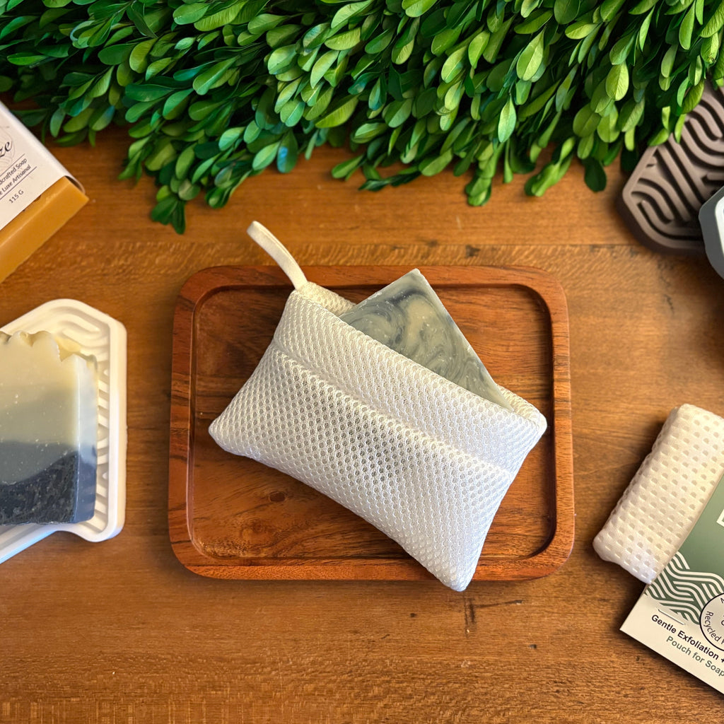 Zero-waste products including a reusable soap bag, bar of soap, and packaging on a wooden surface with greenery.